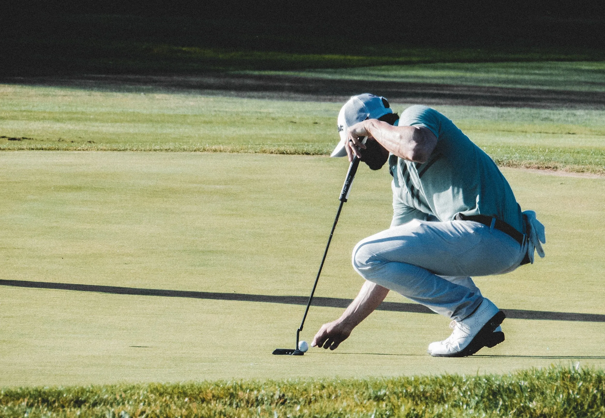 A golfer crouching to read a putt.