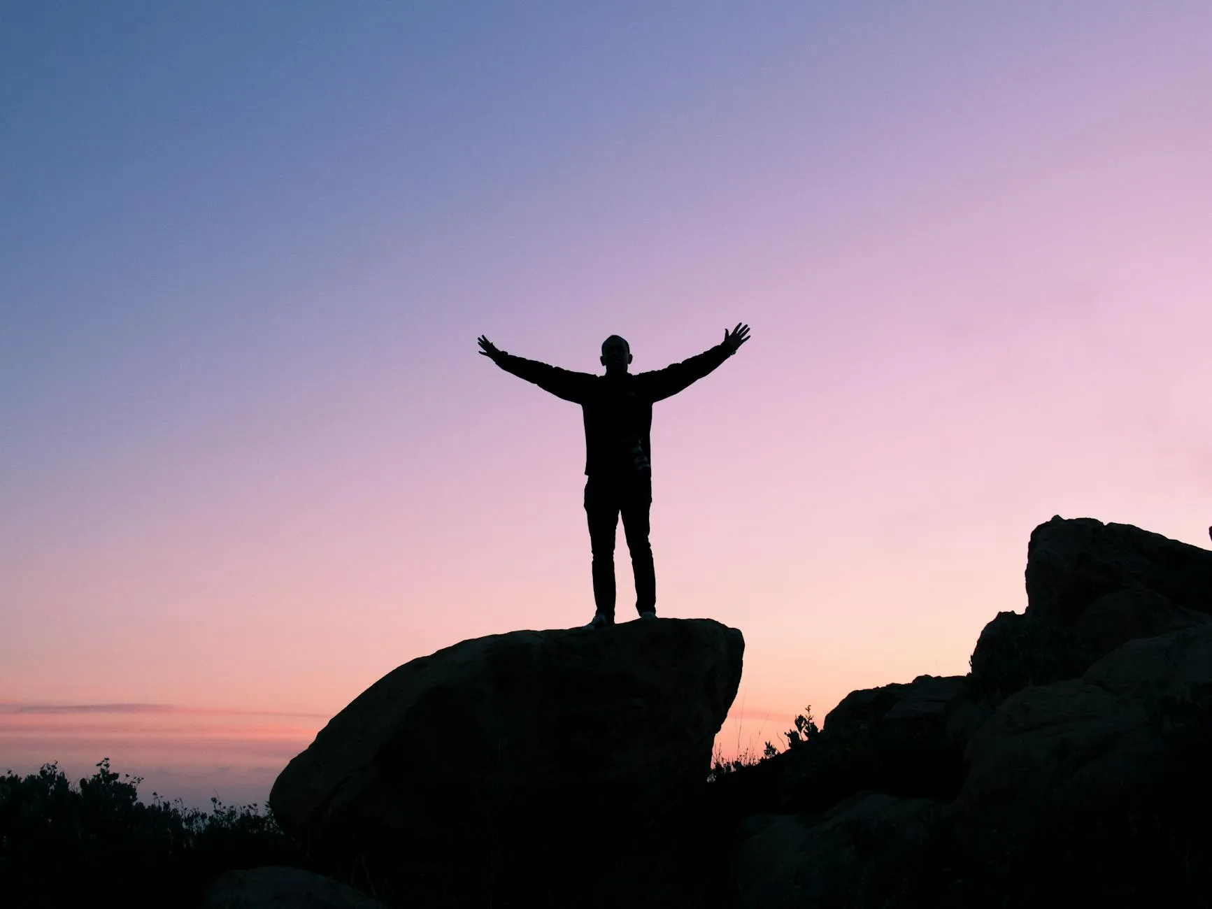 A person on a rock with arms raised at sunset.